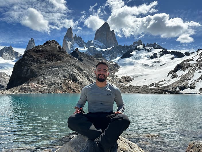 Diego Romero sitting by a lake with mountains in the background